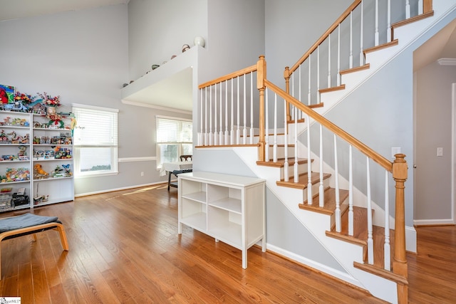 stairs featuring wood finished floors, a towering ceiling, and baseboards