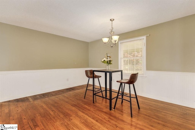 dining room featuring a wainscoted wall, dark wood-type flooring, a textured ceiling, and a notable chandelier