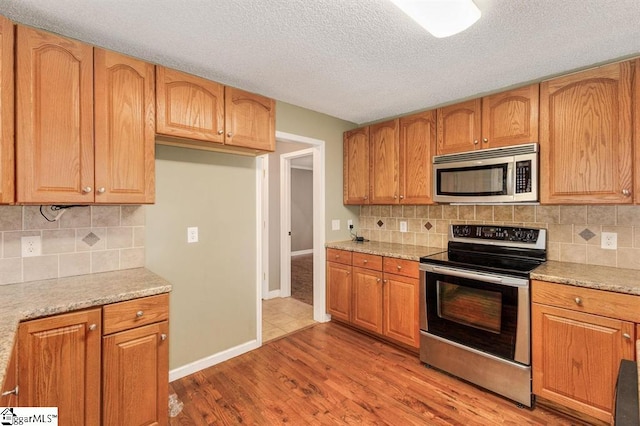 kitchen featuring light stone counters, stainless steel appliances, decorative backsplash, light wood-style floors, and baseboards