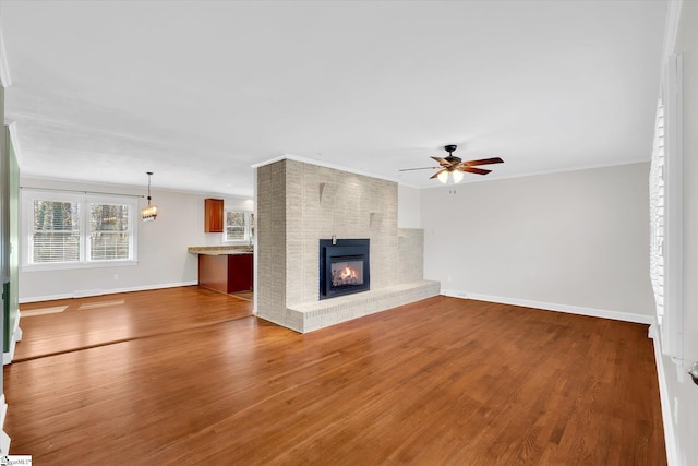 unfurnished living room with a brick fireplace, ceiling fan, baseboards, and wood finished floors