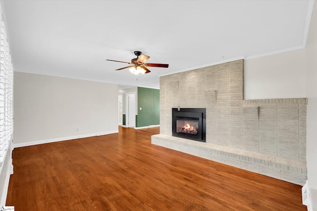 unfurnished living room with a brick fireplace, wood finished floors, a ceiling fan, and baseboards