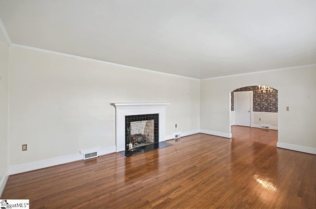 unfurnished living room with arched walkways, crown molding, wood finished floors, a tile fireplace, and baseboards