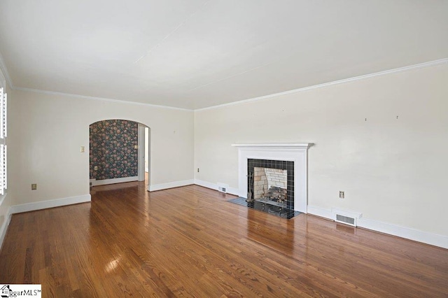 unfurnished living room with visible vents, arched walkways, a tile fireplace, wood finished floors, and crown molding