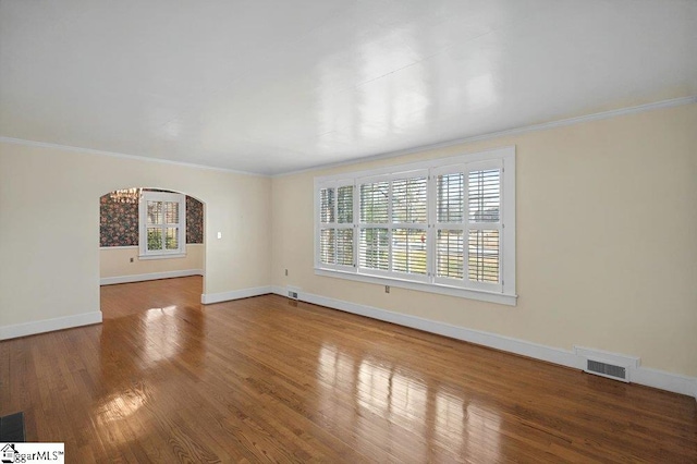 empty room featuring arched walkways, ornamental molding, wood finished floors, and baseboards