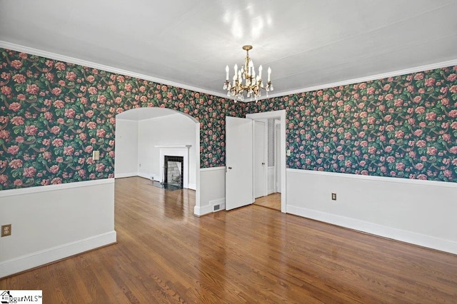 spare room featuring a fireplace with flush hearth, wood finished floors, wainscoting, and wallpapered walls