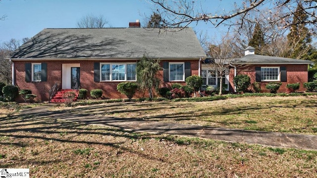 view of front of property featuring brick siding, a chimney, and a front lawn