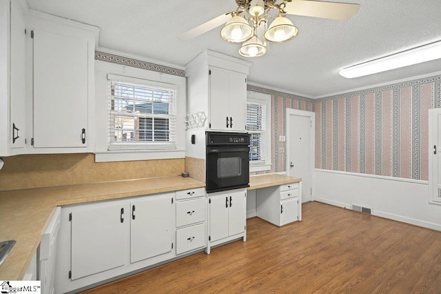 kitchen featuring light countertops, white cabinets, a textured ceiling, black oven, and wallpapered walls