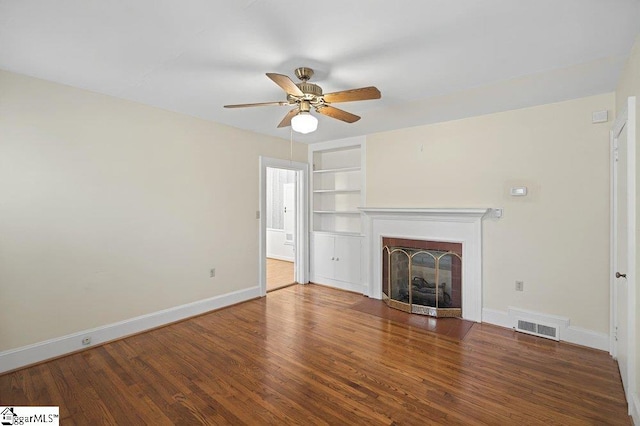 unfurnished living room featuring built in shelves, dark wood finished floors, visible vents, a fireplace with flush hearth, and baseboards