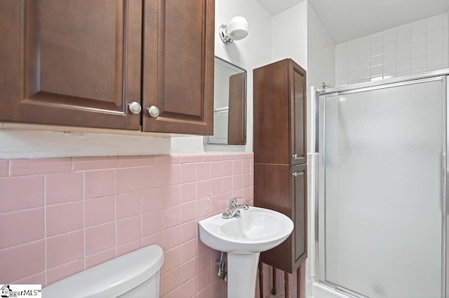 bathroom with toilet, a shower with shower door, and tile walls