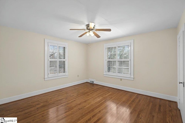 unfurnished room with visible vents, dark wood-type flooring, a ceiling fan, and baseboards