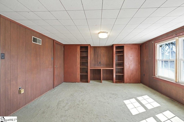 spare room with light colored carpet, visible vents, and wooden walls