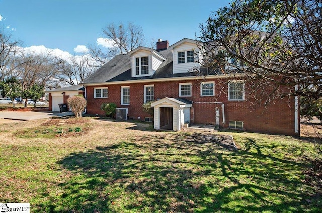 view of front of property featuring brick siding, a chimney, cooling unit, and a front lawn