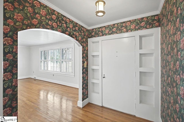 entryway featuring wallpapered walls, crown molding, baseboards, and wood finished floors