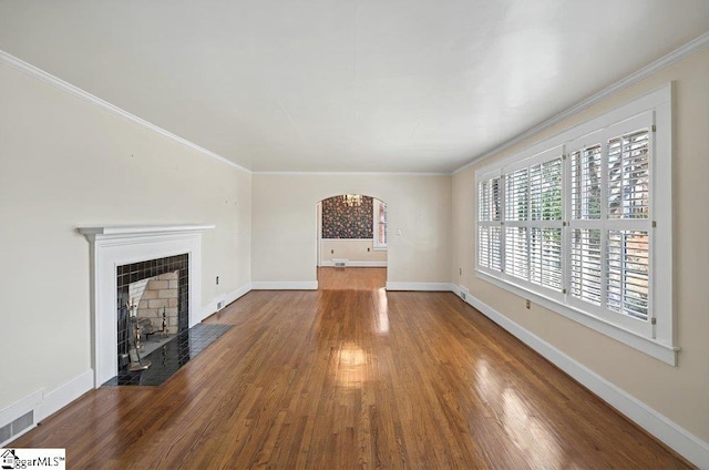 unfurnished living room featuring arched walkways, crown molding, baseboards, and wood finished floors