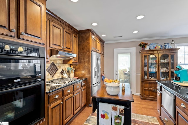 kitchen featuring decorative backsplash, dark countertops, appliances with stainless steel finishes, ornamental molding, and under cabinet range hood