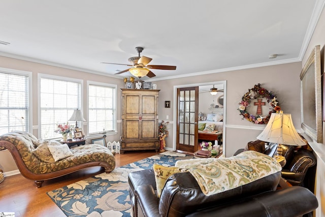 living room featuring baseboards, visible vents, a ceiling fan, ornamental molding, and light wood-type flooring