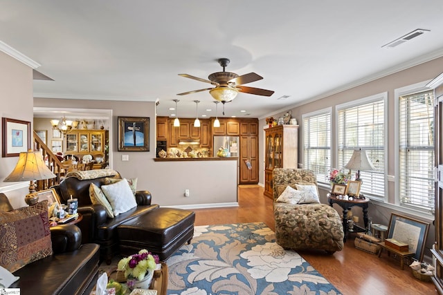 living area with ceiling fan with notable chandelier, ornamental molding, visible vents, and light wood-style floors