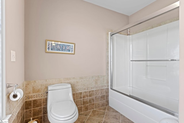 full bathroom featuring wainscoting, toilet, tile patterned flooring, combined bath / shower with glass door, and tile walls