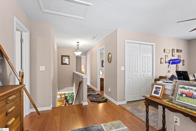 hall featuring baseboards, wood finished floors, an upstairs landing, and attic access