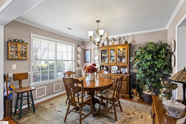 dining room with visible vents, a wainscoted wall, an inviting chandelier, crown molding, and a decorative wall