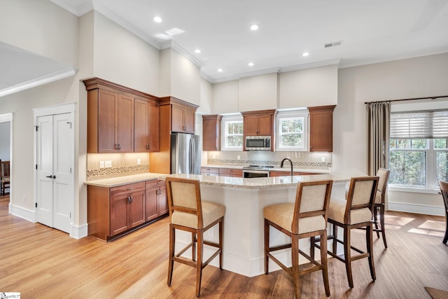 kitchen with light stone counters, brown cabinets, visible vents, appliances with stainless steel finishes, and a kitchen island with sink