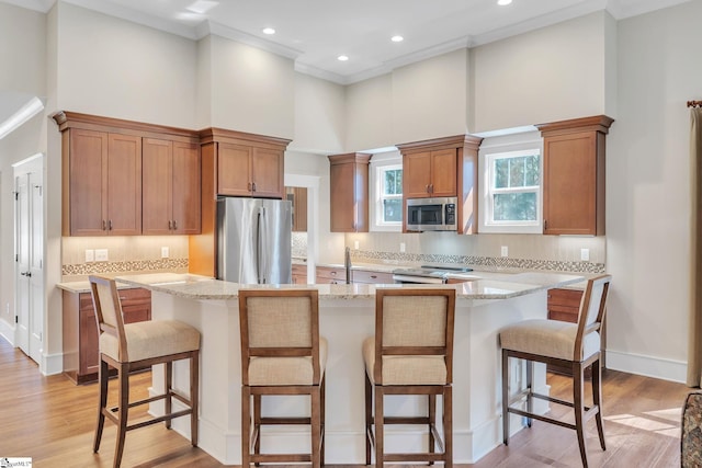 kitchen with stainless steel appliances, light stone counters, brown cabinetry, and a center island