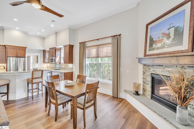 dining space with visible vents, light wood-style floors, ornamental molding, a stone fireplace, and baseboards