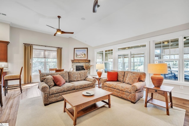 living area featuring light wood finished floors, visible vents, a ceiling fan, lofted ceiling, and a stone fireplace