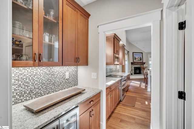 kitchen featuring stainless steel appliances, light wood-type flooring, glass insert cabinets, and light stone countertops