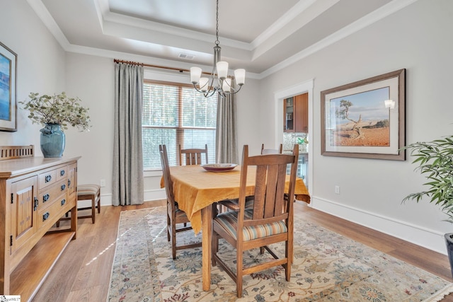 dining area with light wood-type flooring, a raised ceiling, and baseboards