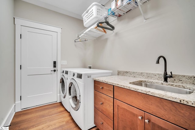 laundry area featuring light wood-style flooring, cabinet space, a sink, and washer and clothes dryer