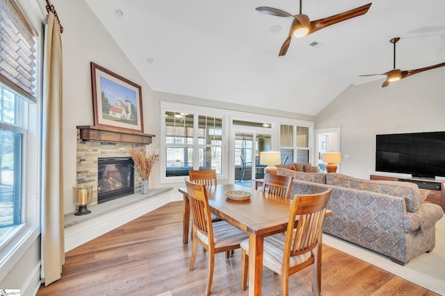 dining area featuring light wood finished floors, visible vents, a ceiling fan, a stone fireplace, and high vaulted ceiling