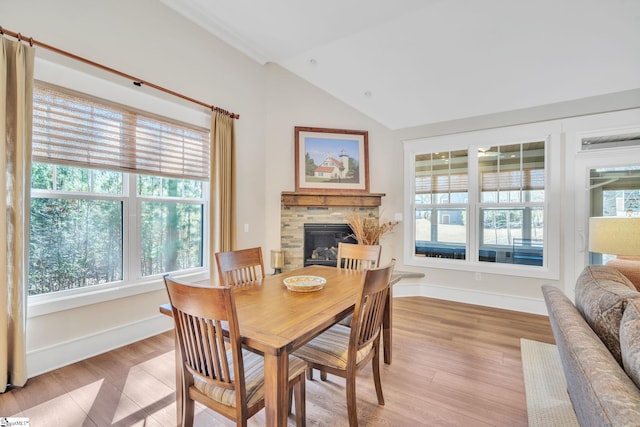 dining space with light wood-style floors, a glass covered fireplace, vaulted ceiling, and baseboards