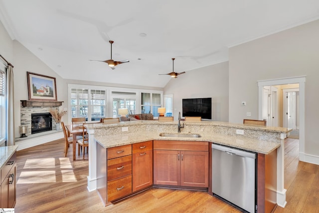 kitchen featuring stainless steel dishwasher, brown cabinetry, a glass covered fireplace, open floor plan, and a sink