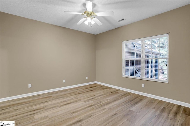 spare room featuring a textured ceiling, visible vents, baseboards, a ceiling fan, and light wood-style floors