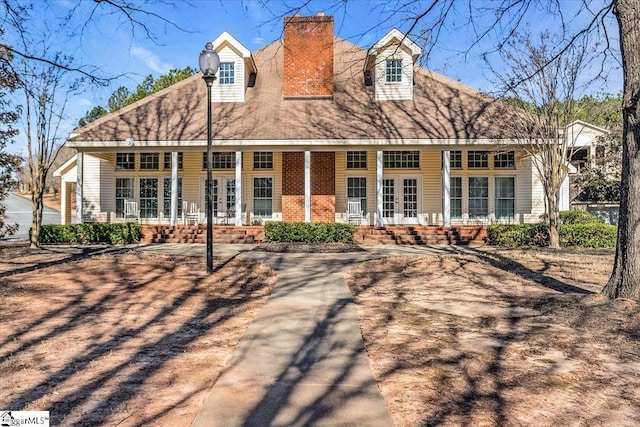 back of house with covered porch, a chimney, and brick siding