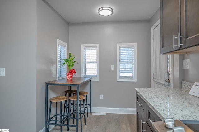 kitchen with dark brown cabinetry, baseboards, light stone counters, and light wood-style floors