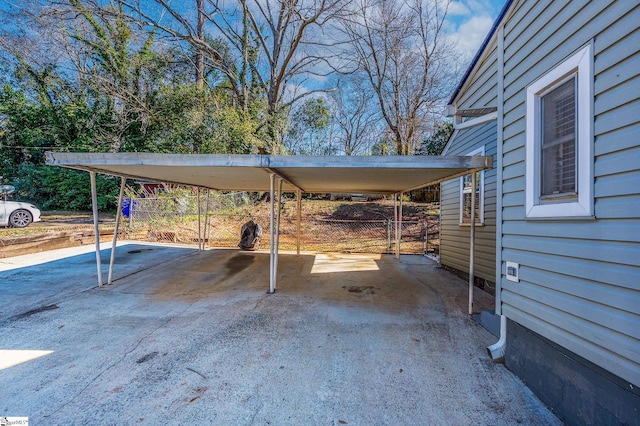 view of parking with driveway, a carport, and fence