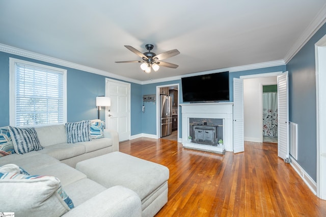 living room featuring visible vents, a fireplace with raised hearth, ceiling fan, wood finished floors, and crown molding