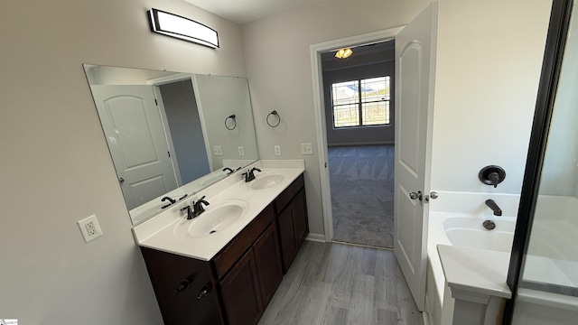 full bathroom with double vanity, baseboards, a sink, and wood finished floors