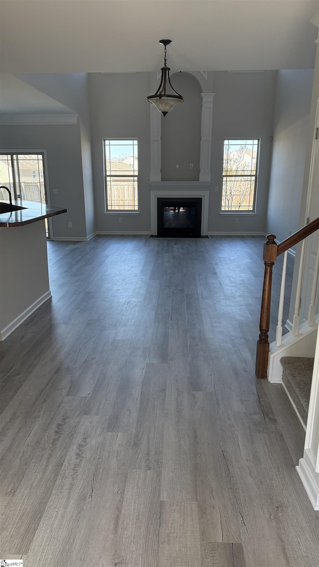 unfurnished living room featuring a glass covered fireplace, wood finished floors, a healthy amount of sunlight, and stairs