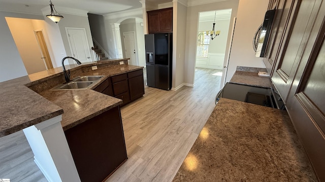 kitchen with light wood-style flooring, a sink, ornamental molding, black fridge, and decorative light fixtures