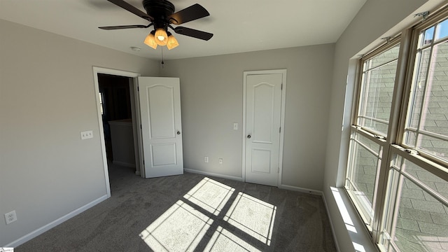 unfurnished bedroom with ceiling fan, dark colored carpet, and baseboards