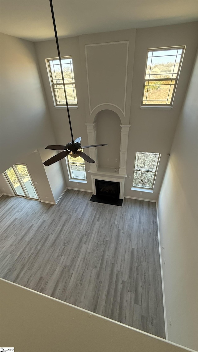 unfurnished living room featuring baseboards, a towering ceiling, ceiling fan, a fireplace with flush hearth, and wood finished floors