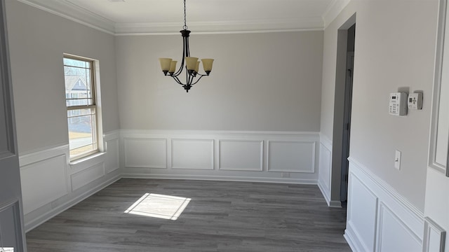 unfurnished dining area with dark wood finished floors, a notable chandelier, and crown molding