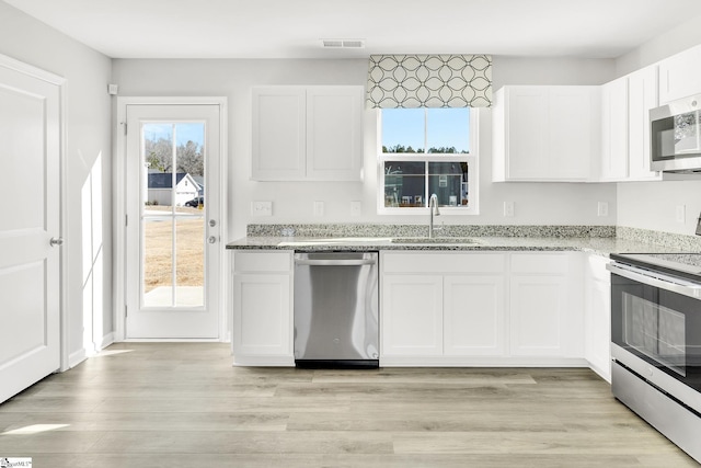 kitchen featuring light stone countertops, visible vents, light wood finished floors, a sink, and appliances with stainless steel finishes