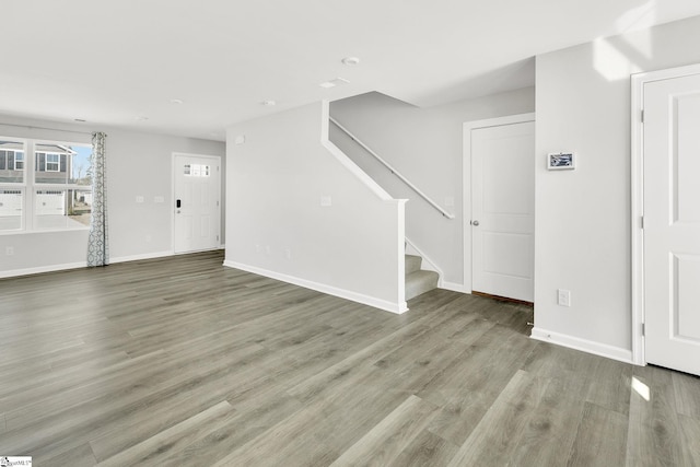 unfurnished living room with baseboards, wood finished floors, and stairs