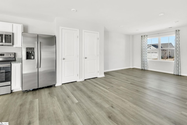 kitchen featuring light stone counters, baseboards, stainless steel appliances, white cabinets, and light wood-style floors