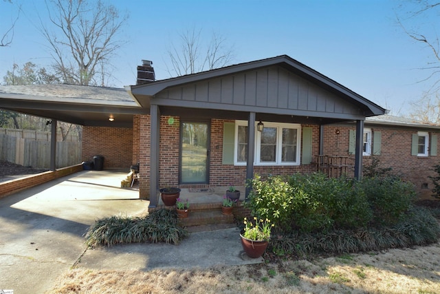 view of front of house featuring concrete driveway, a chimney, fence, a carport, and brick siding