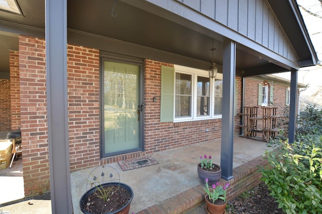 view of exterior entry with a porch, board and batten siding, and brick siding